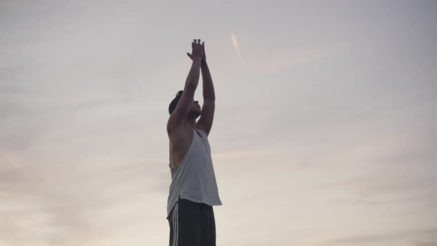 A man standing on grass stretching with the sky and clouds in the background