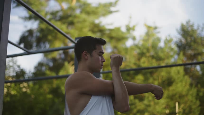 A man does arm stretches while standing outdoors during the day