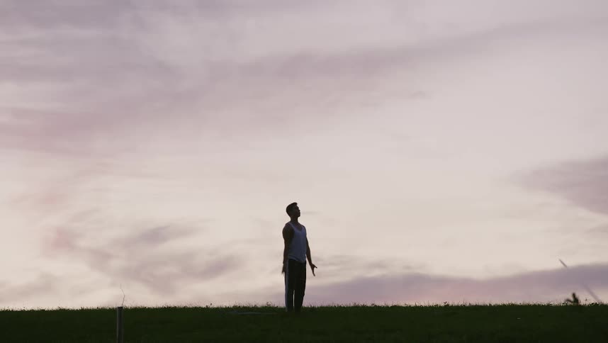 Silhouette of a young man doing yoga and stretching against the evening sky