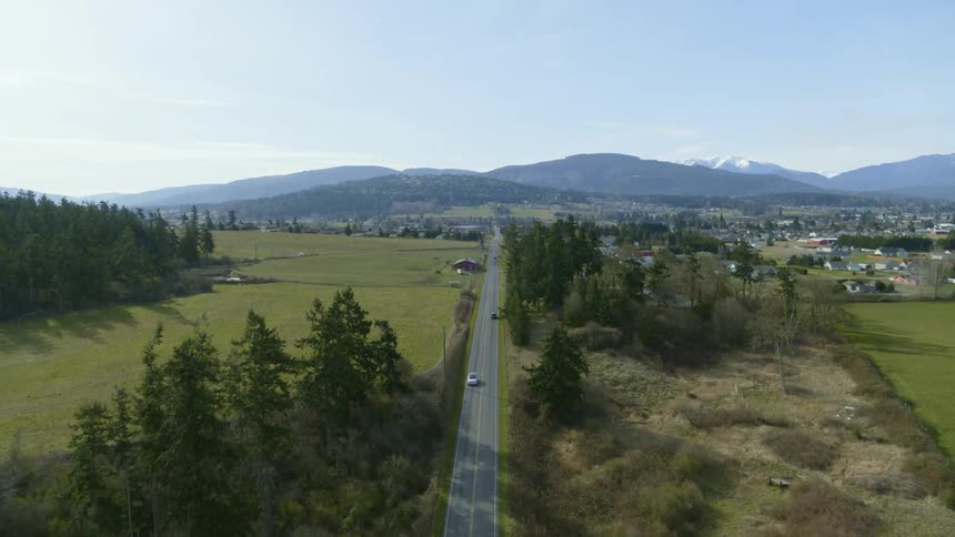 Traverse along a country road with a small town and snow covered mountains in the distance