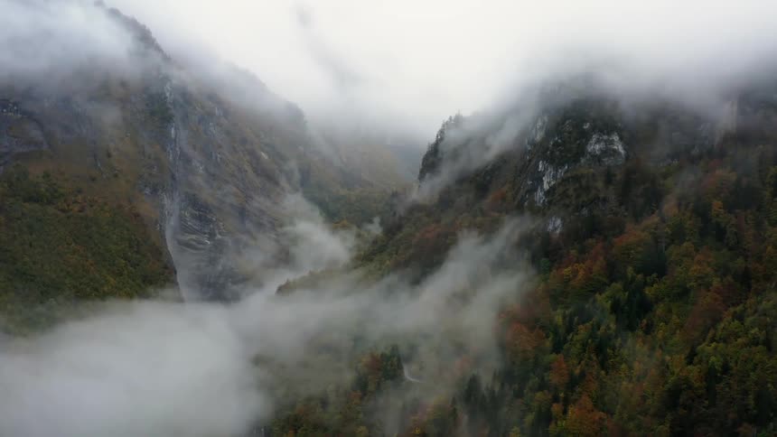 An aerial view of a forested mountain and valley with fog and low clouds during the fall season