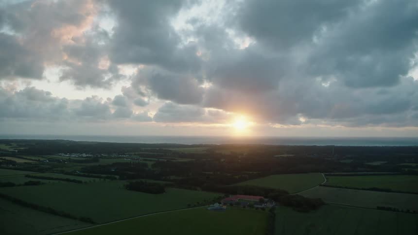 Sun shine from just above horizon onto fields and forest in countryside