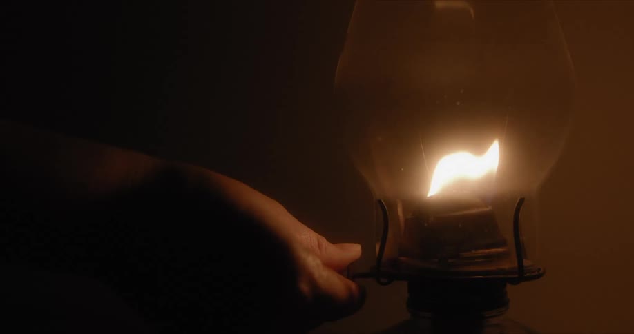 As a flame inside a lamp burns a hand turns it off and the room is dark