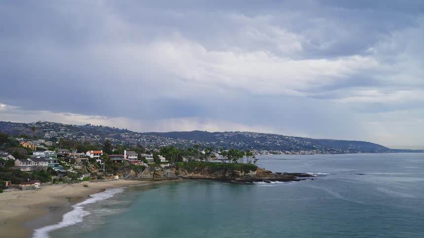 Waves crash onto beach near mist covered town under overcast sky