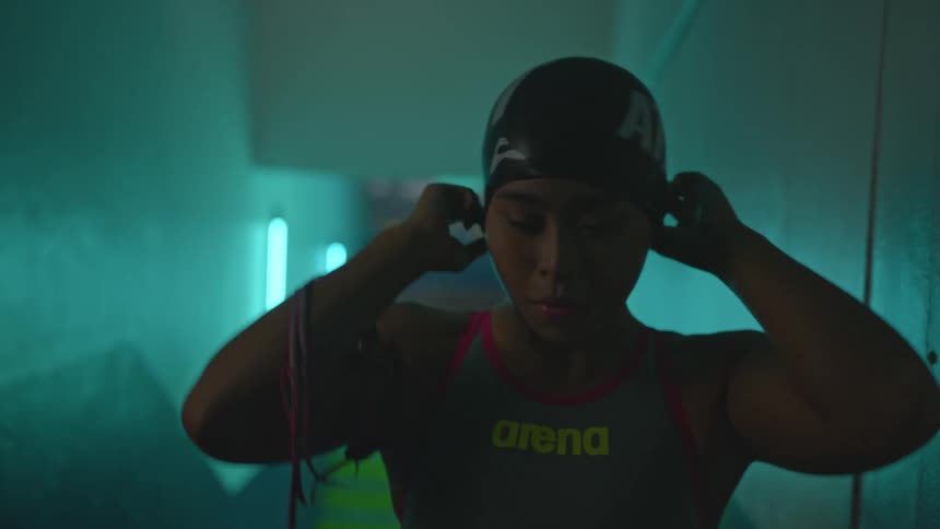 Young woman standing in a hallway under blue lights puts a swimming cap