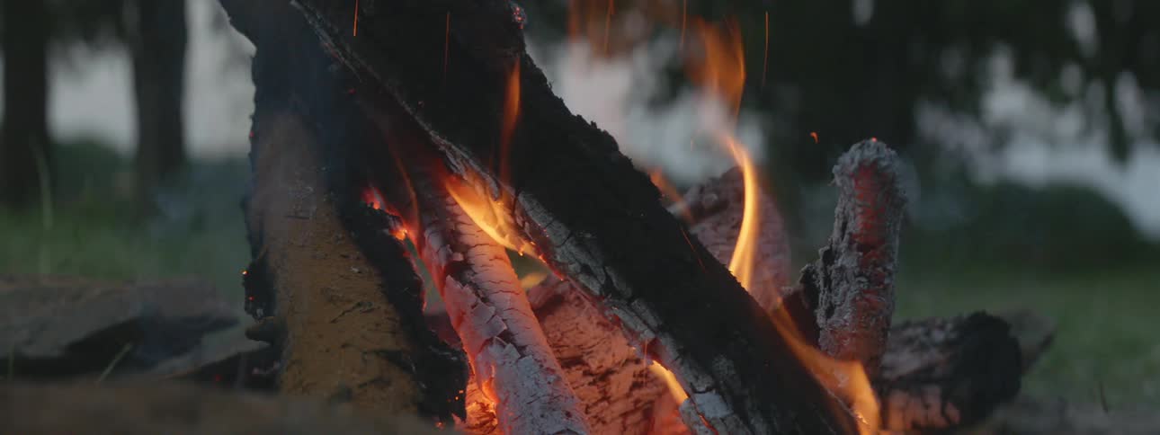 Sparks fly as flames are burning the charred wood of a campfire