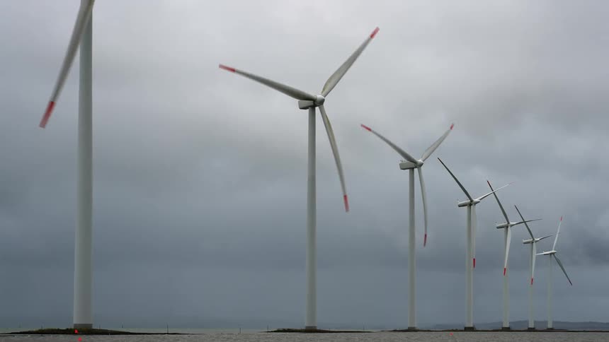 Wind turbines spin on a wind farm under a cloudy sky