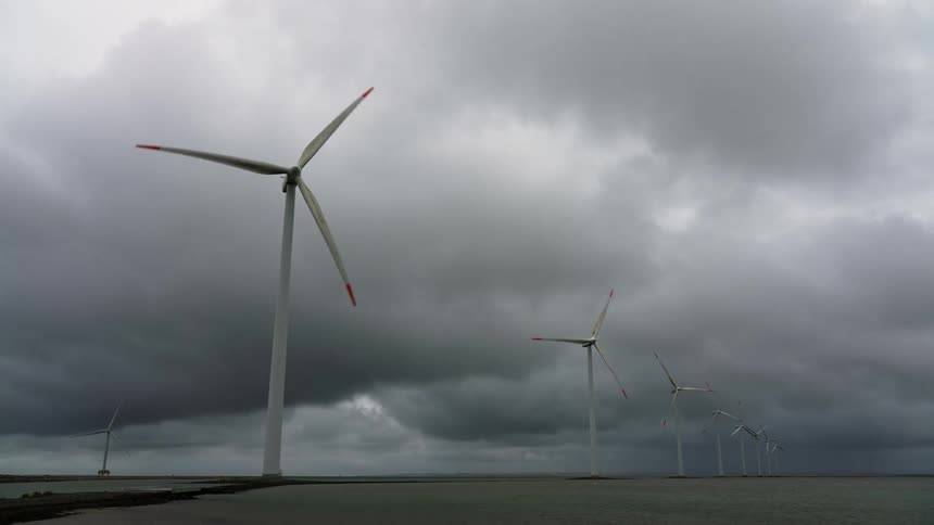 Wind turbines spin on a wind farm under a cloudy sky