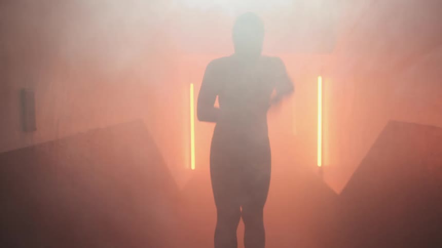 Young woman wearing swimming gear stretches walking on a hallway filled with smoke and flashing orange lights