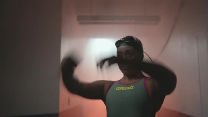 Female swimmer preps and stretches as smoke rises and red light flickers behind her