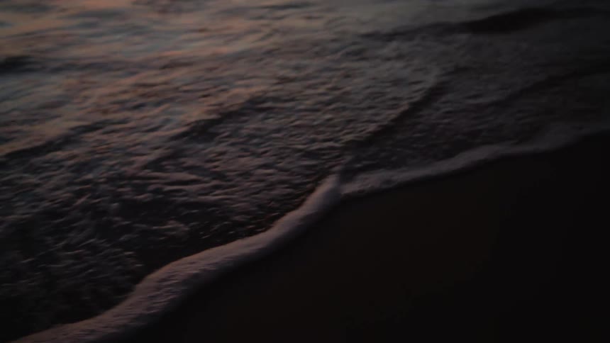 Small ocean waves washing over the wet sand on the beach at sunset