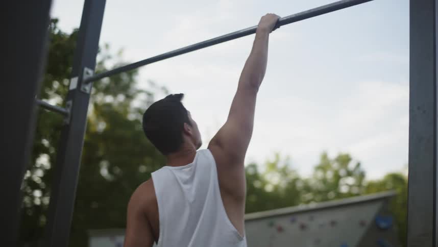 Man exercises on metal bar in park with climbing wall in background