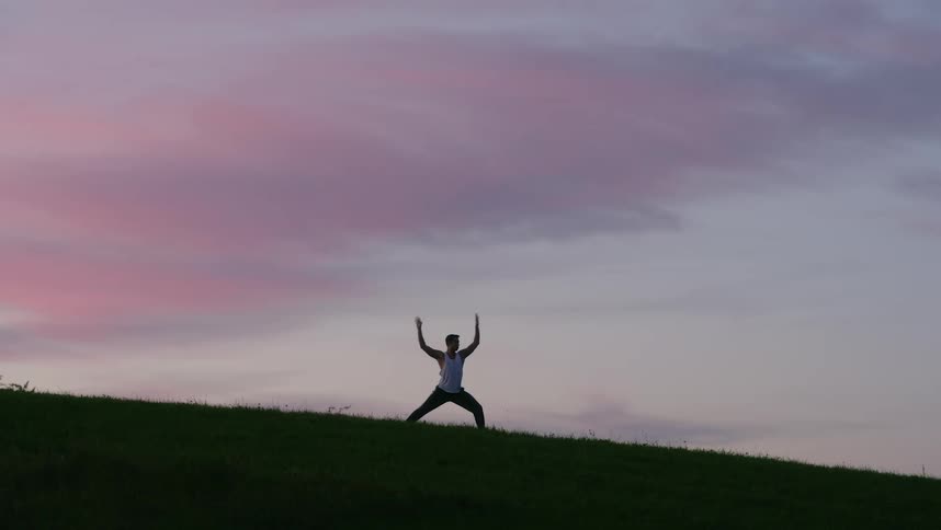Silhouette of a man doing tai chi movements with pink clouds above him