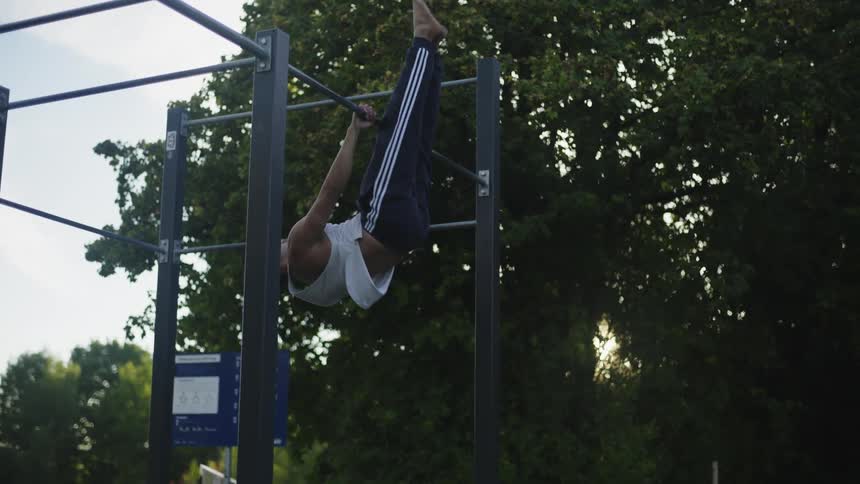 Man exercise on metal bars in park as sun shines through nearby trees