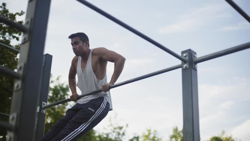 Man exercises on metal bar outdoors near wall under cloudy sky