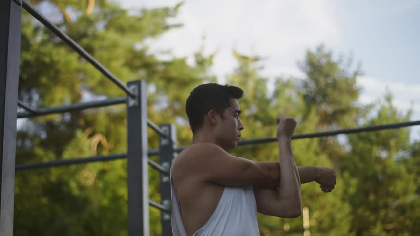 A man is outdoors at a park stretching his arms in the daytime
