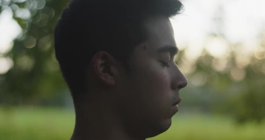 Young man sitting over the grass on a yoga pose meditating at evening