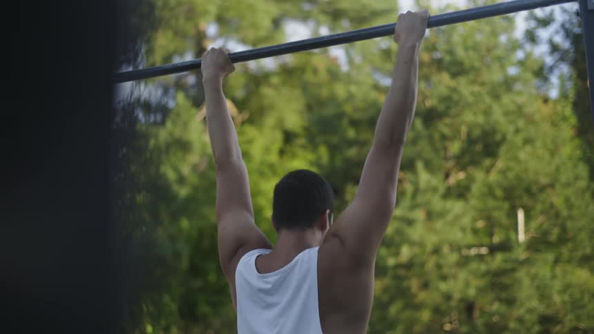 A man is doing pull ups in the park