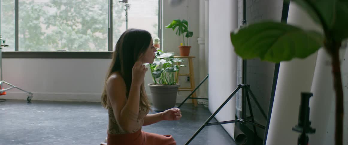 Woman puts on earring sitting on floor near mirror in studio