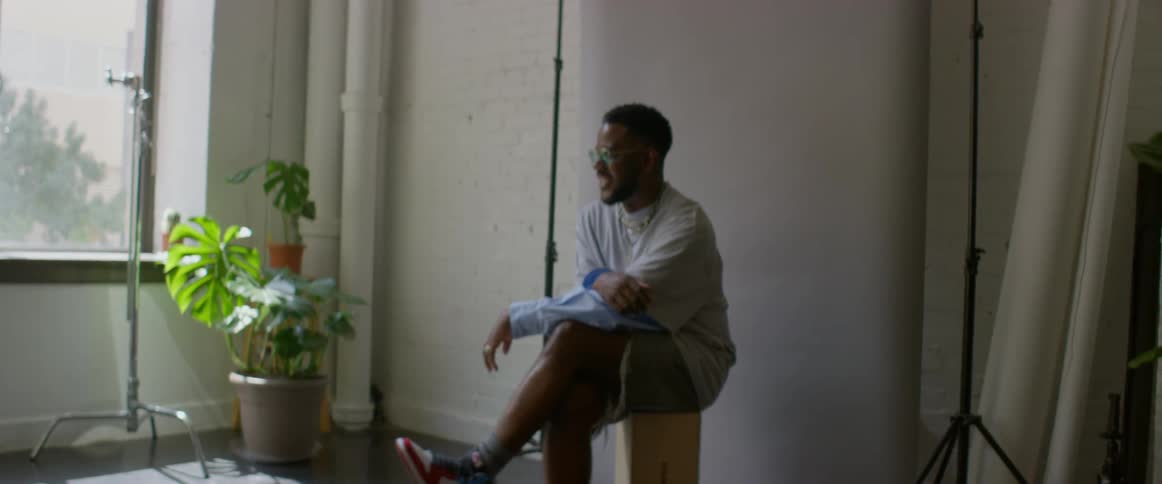 Photographer takes pictures of a male model sitting in front of a white brick wall