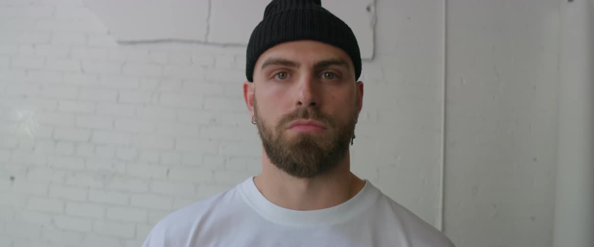 A man with a beard and wearing a black stocking hat turns his head and looks forward