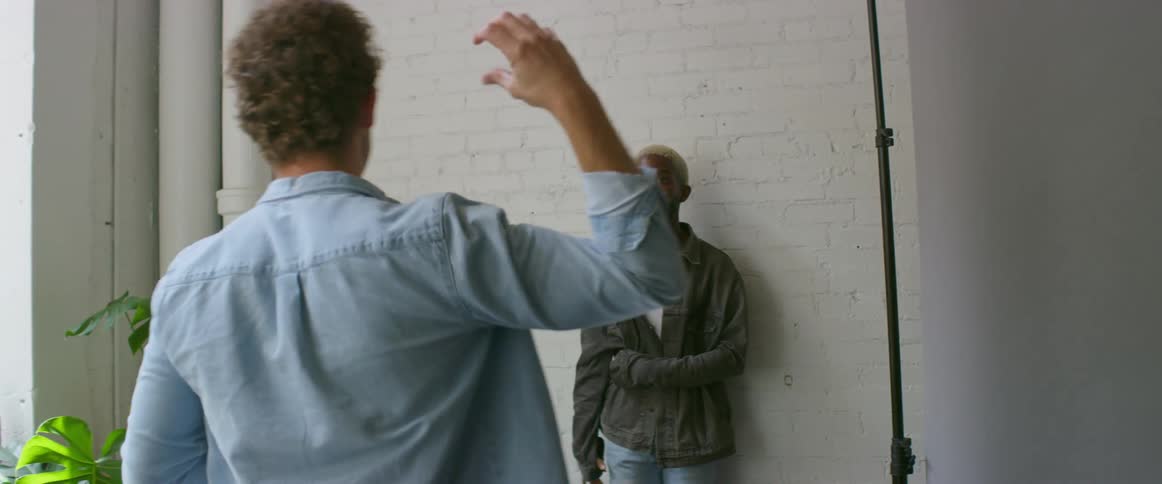 Photographer takes pictures of a male model in front of a white brick wall