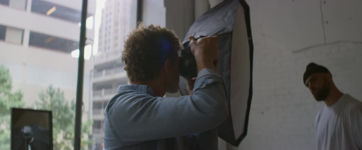 A photographer checks his camera and moves in for a closer shot of a man posing against a wall