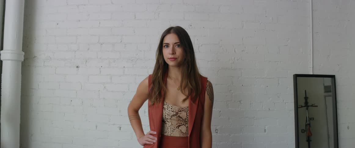 Woman poses against white painted brick wall near mirror