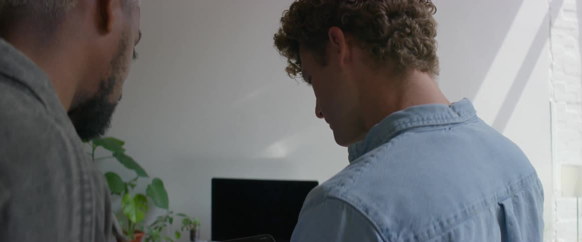 Two men in a room looking at a tablet with a wall and window in the background