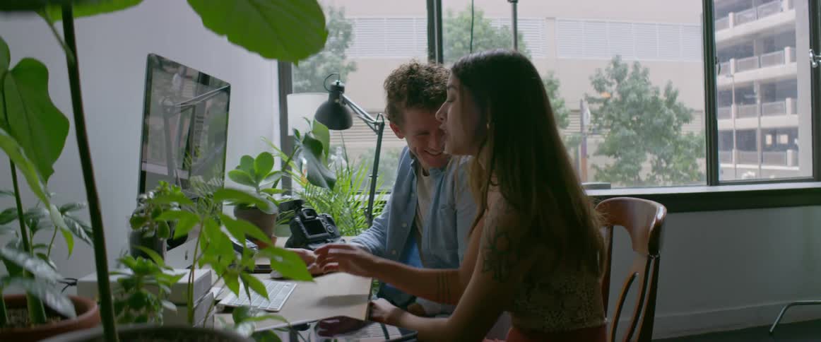 A man and a woman are indoors working at a computer during the daytime