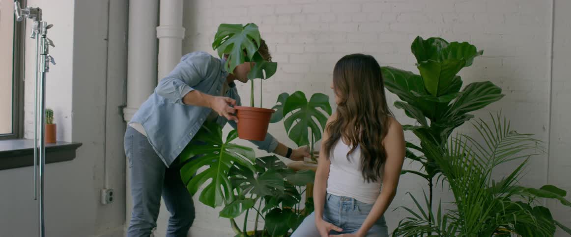 Photographer arranging plants around a female model for a photoshoot inside an apartment