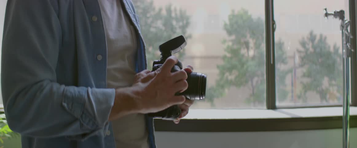 A man looks through his dslr camera while standing in his living room
