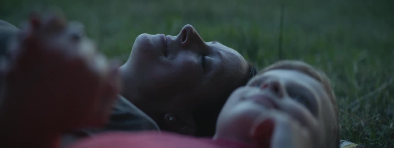 Mother and son laying on the green grass looking at the sky at evening