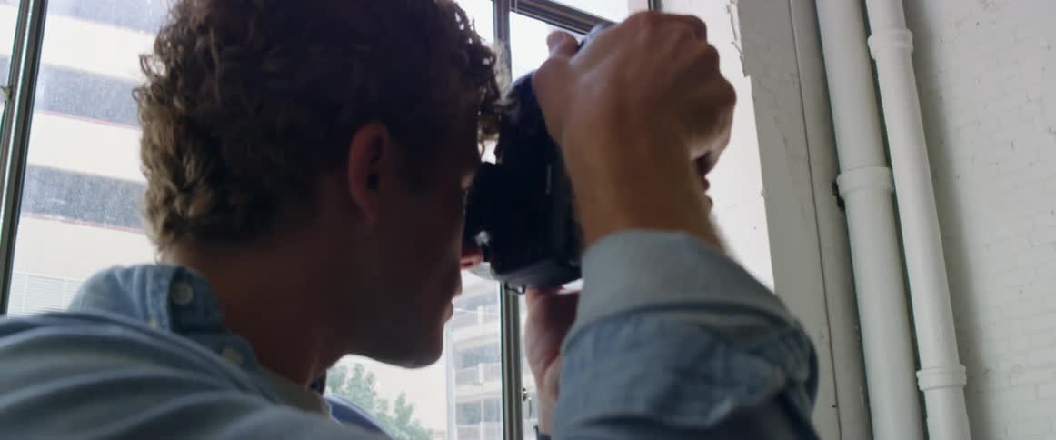 Photographer uses a camera to take pictures of a young female model against a white wall in the city