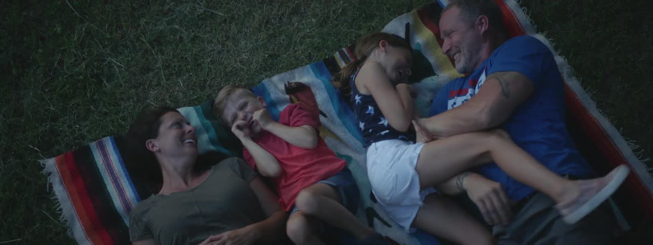 A man tickles his daughter and son as the family lies on a blanket outside
