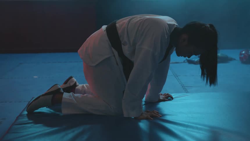 A woman practicing martial arts with a shelf trophies and a wall in the background