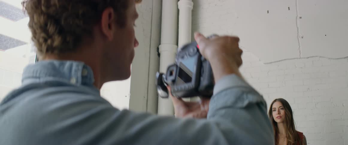 A man in a room with a camera taking a picture of a woman with a wall in the background