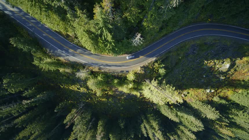 Dynamic reveal of a winding mountain road as a car drives around a bend