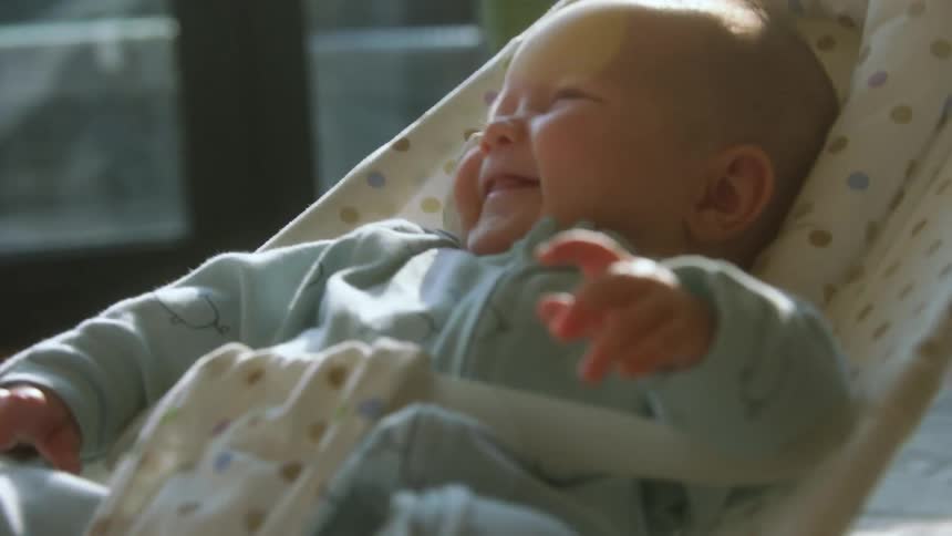 Baby toddler rocking on a baby chair near a window smiling