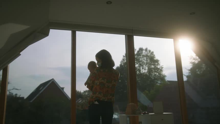 Mother holding her baby while standing on the living room at home