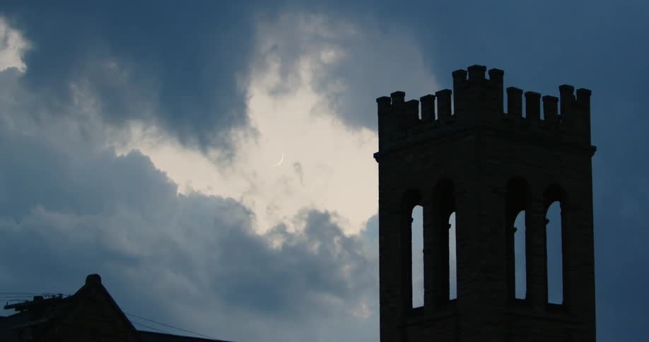 The silhouette of a bell tower with battlements against a gray cloud sky