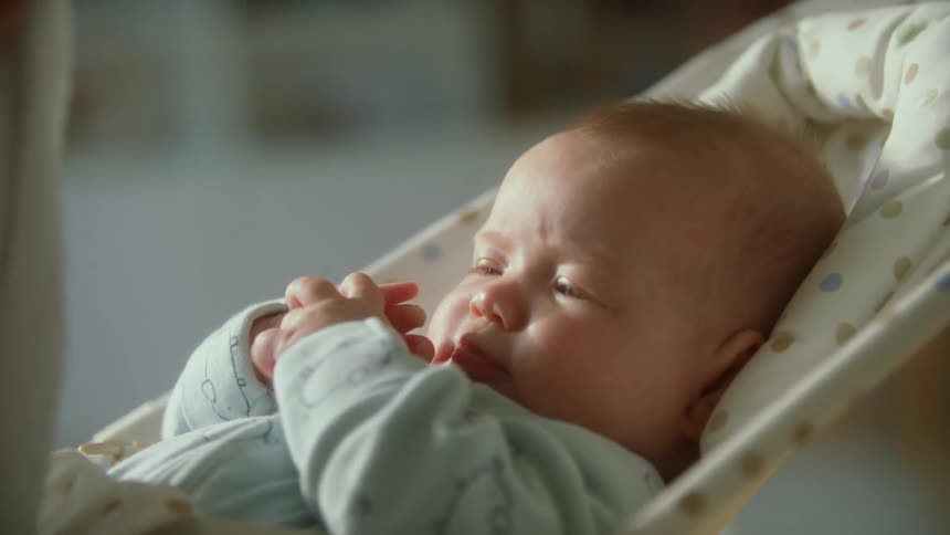 Mother rubs forehead of her baby while he sleeps in a baby chair at home