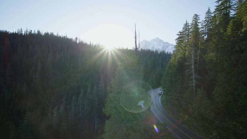 Chasing behind a white SUV driving up a mountain highway as the sun rises over the trees