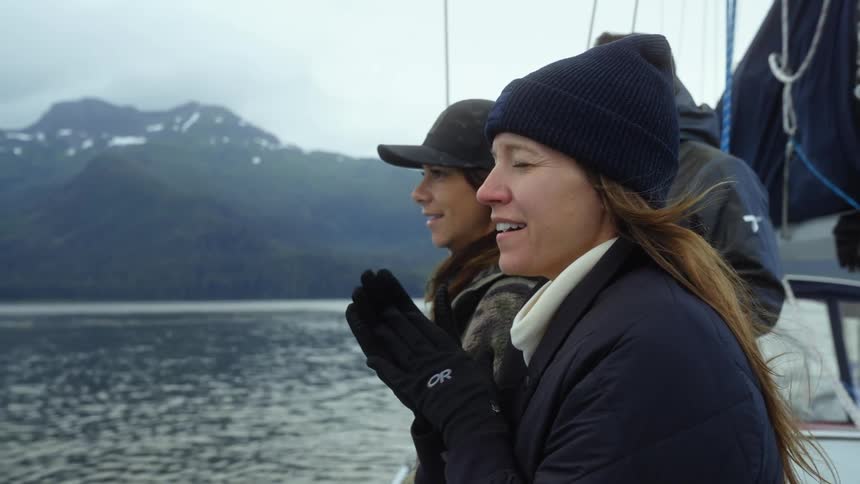 Group of friends standing on a yatch waiting while looking at the ocean near the mountain
