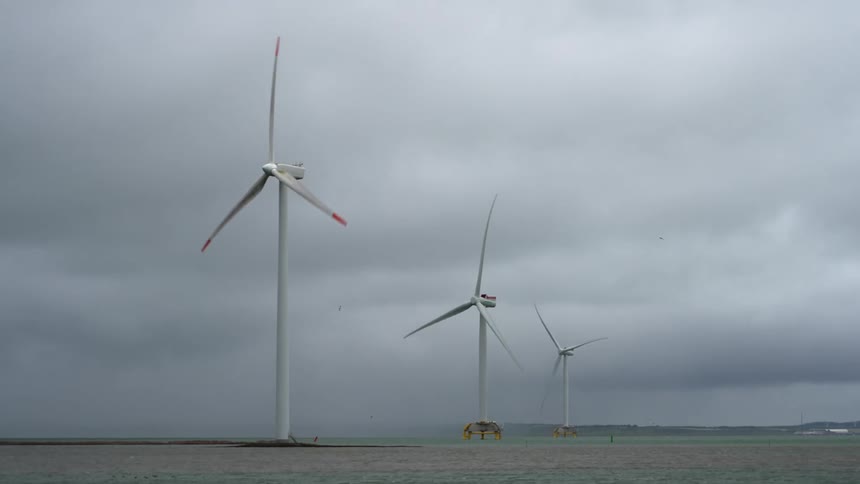 Wind turbines spin on a wind farm under a cloudy sky