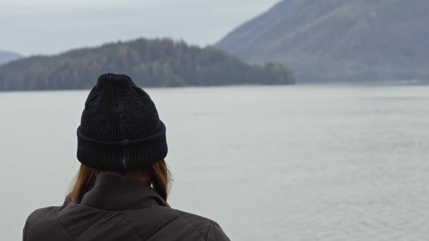 Woman wearing a jacket and beanie looking at a lake in the mountains