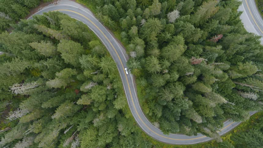 Top down tracking shot of a white car driving up multipe S curves on a mountain road