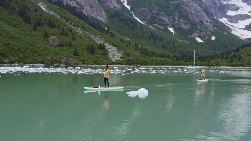 Two people are surfboard rowing in the icy lake