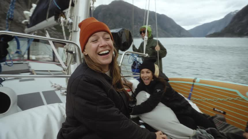 Group of happy friends smile and laugh over a boat in a lake near the mountains