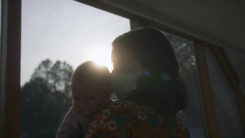 A mother is holding her baby by the window